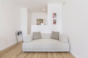 Ein schlichter Wohnraum mit einem hellen Sofa, einem kleinen Beistelltisch und einem Garderobenschrank.