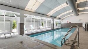 An indoor swimming pool with clear glass walls, lounge chairs, and a modern ceiling design. - Yarra Edge River and Skyline Views with Shared Pool (Melbourne)