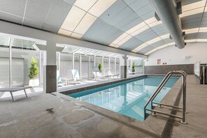 Ein Innenpool mit großen Glaswänden, Liegestühlen und einem modernen Deckenbau.