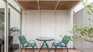 A patio with a round table and two chairs, a glass door, and a plant. - Yarra Edge River and Skyline Views with Shared Pool (Melbourne)