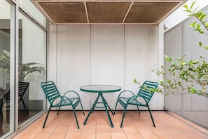Eine Terrasse mit einem runden Tisch, zwei Stühlen, einer Glastür und einer Pflanze.