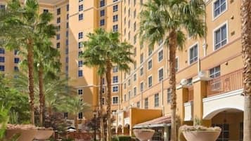 A multi-story hotel with a central courtyard, palm trees, and a paved walkway.