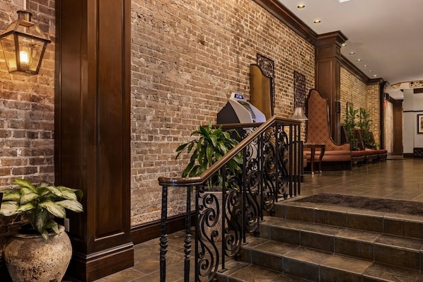 A lobby with a brick wall, a staircase with ornate railings, and an ATM machine.