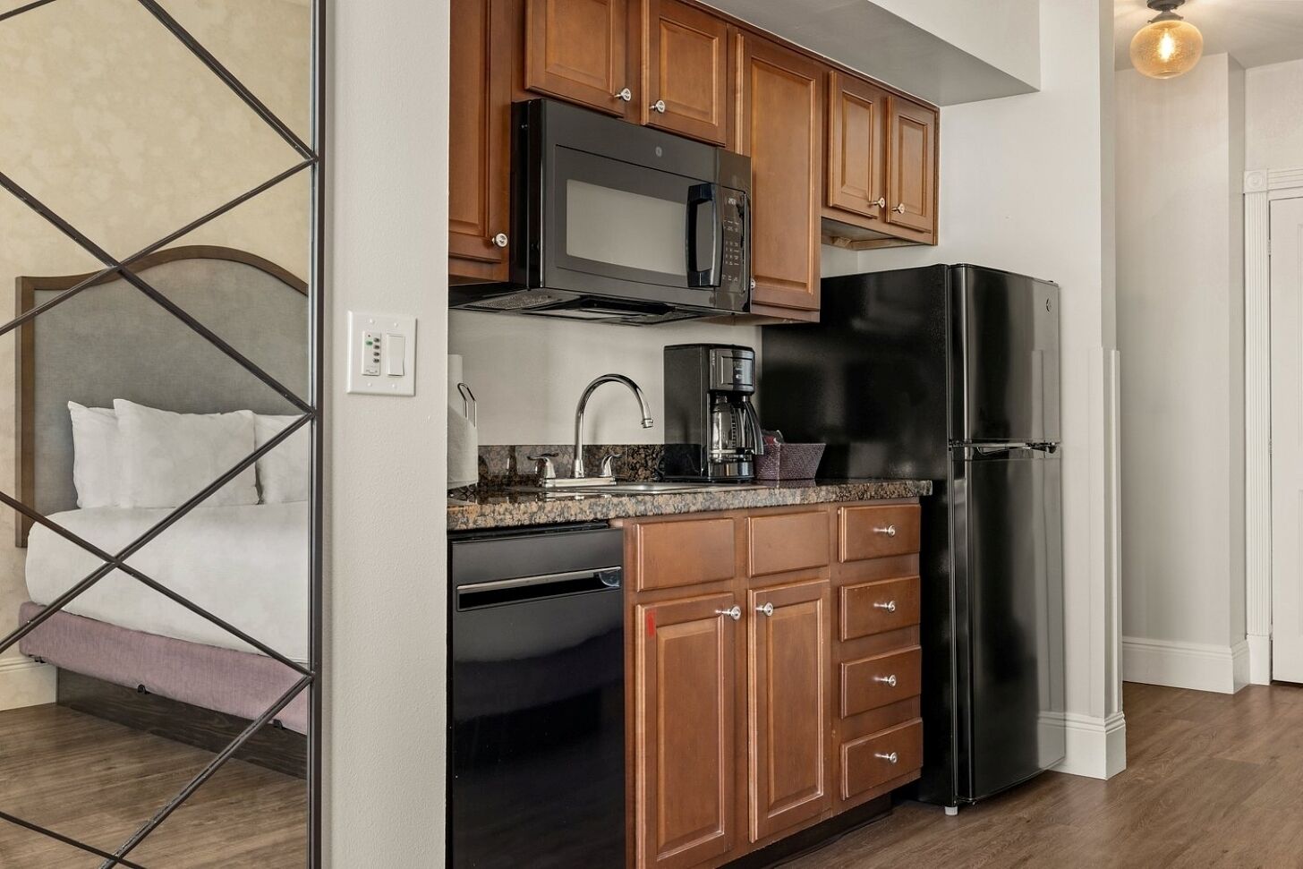 A compact kitchen with wooden cabinets, a black refrigerator, a microwave, and a coffee maker.