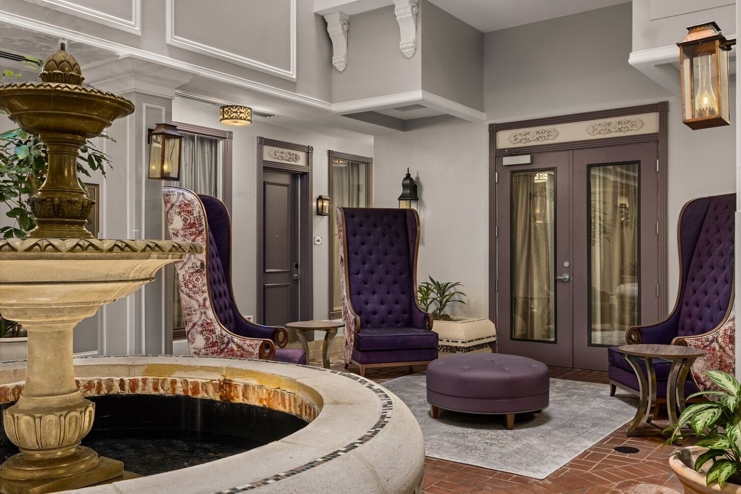 A lobby with a fountain, two purple armchairs, a small ottoman, and a door with a sign.