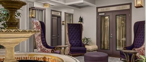 A lobby with a fountain, two purple armchairs, a small ottoman, and a door with a sign.