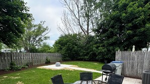 Eine Terrasse im Freien mit einem Glastisch und schwarzen Korbstühlen, umgeben von einem Holzzaun und Pflanzen.