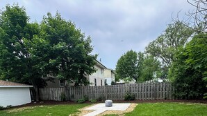 Ein Garten mit Rasenfläche, einem Betonweg und einem Holzzaun.