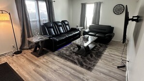 Ein Wohnzimmer mit einem schwarzen Ledersofa, einem Couchtisch und einem flachbildfernseher an der Wand.