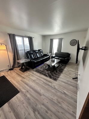 Ett vardagsrum med en svart lädersoffa, ett soffbord och en platt-TV som är monterad på väggen.