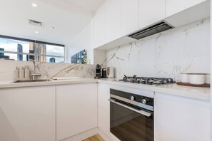 Eine moderne Küche mit weißen Schränken, einer Marmor-Spritzschutzwand, einem Gasherd und einem Backofen.