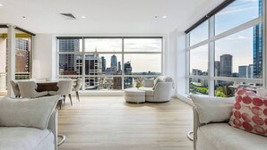 Uma sala de estar ampla com vista para a cidade, um espaço de refeições com mesa e cadeiras, e uma área de estar com sofá e poltronas.