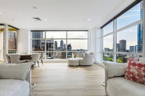 Ein geräumiges Wohnzimmer mit Blick auf die Stadt, ein Essbereich mit Tisch und Stühlen sowie eine Sitzecke mit Sofa und Sesseln.