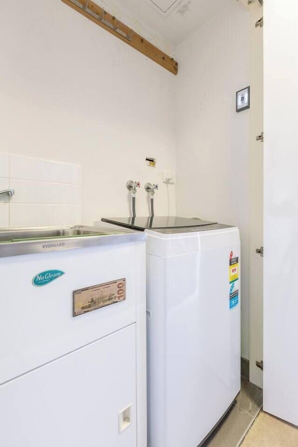 A laundry area with a NuGleam branded washing machine and dryer, a stainless steel sink, and a wooden beam ceiling.
