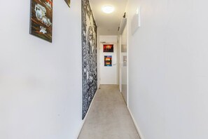 A narrow hallway with white walls, a patterned tapestry, and two framed pictures on the walls.