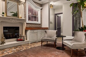 A room with a fireplace, two armchairs, a small table, and a window with decorative items.