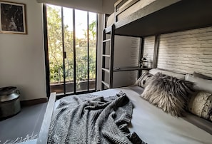 Ein Stockbett mit Blick auf Bäume durch ein Fenster, ein Nachttisch und eine Lampe.