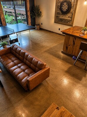 A spacious room with a brown leather sofa, a dartboard, and a ping pong table. - "Starlake" A huge waterfront 5 bedroom estate only 15min to downtown Blueridge. (Mineral Bluff)