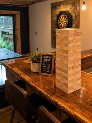 A tabletop Jenga game set up on a wooden bar counter with a sign instructing players. - "Starlake" A huge waterfront 5 bedroom estate only 15min to downtown Blueridge. (Mineral Bluff)