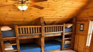 Eine Holzhütte mit Etagenbetten, einem Deckenventilator und einem Fenster mit Jalousien.