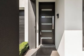 A modern exterior with a dark door, a small entryway, and a wall-mounted light fixture. - The Pool Pavilion Where City meets Beach (Bentleigh)