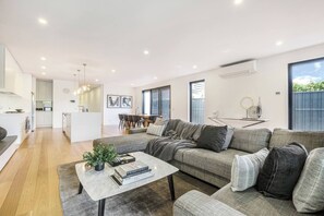 Ein modernes Wohnzimmer mit einem grauen Sofa, einem Couchtisch und einem Essbereich im Hintergrund.