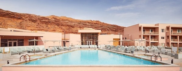 A pool area with lounge chairs, a building with a modern design, and a mountainous backdrop. - Moab | Adventure Desert Retreat | Pool + Hot Tub (Moab)