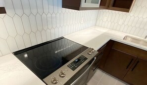 A kitchen with a black induction cooktop, a digital control panel, wooden cabinets, and white hexagonal tiles.