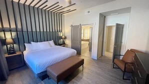 Une chambre d’hôtel moderne dotée d’un grand lit, de tables de chevet, d’un banc, d’une chaise et d’un dressing.
