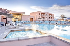 A swimming pool with lounge chairs, a poolside area, and a building with balconies. - Moab | Adventure Desert Retreat | Pool + Hot Tub (Moab)