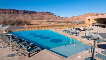 A pool with lounge chairs, a poolside area, and a mountain backdrop.
