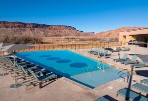 A pool with lounge chairs, a poolside area, and a mountain backdrop. - Moab | Adventure Desert Retreat | Pool + Hot Tub (Moab)