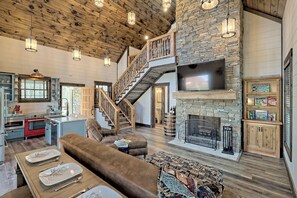 Amplia sala de estar con chimenea de piedra, una escalera de madera y una cocina equipada con electrodomésticos modernos.