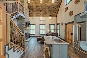 Una cocina amplia con una isla central, una chimenea de piedra y una escalera de madera.