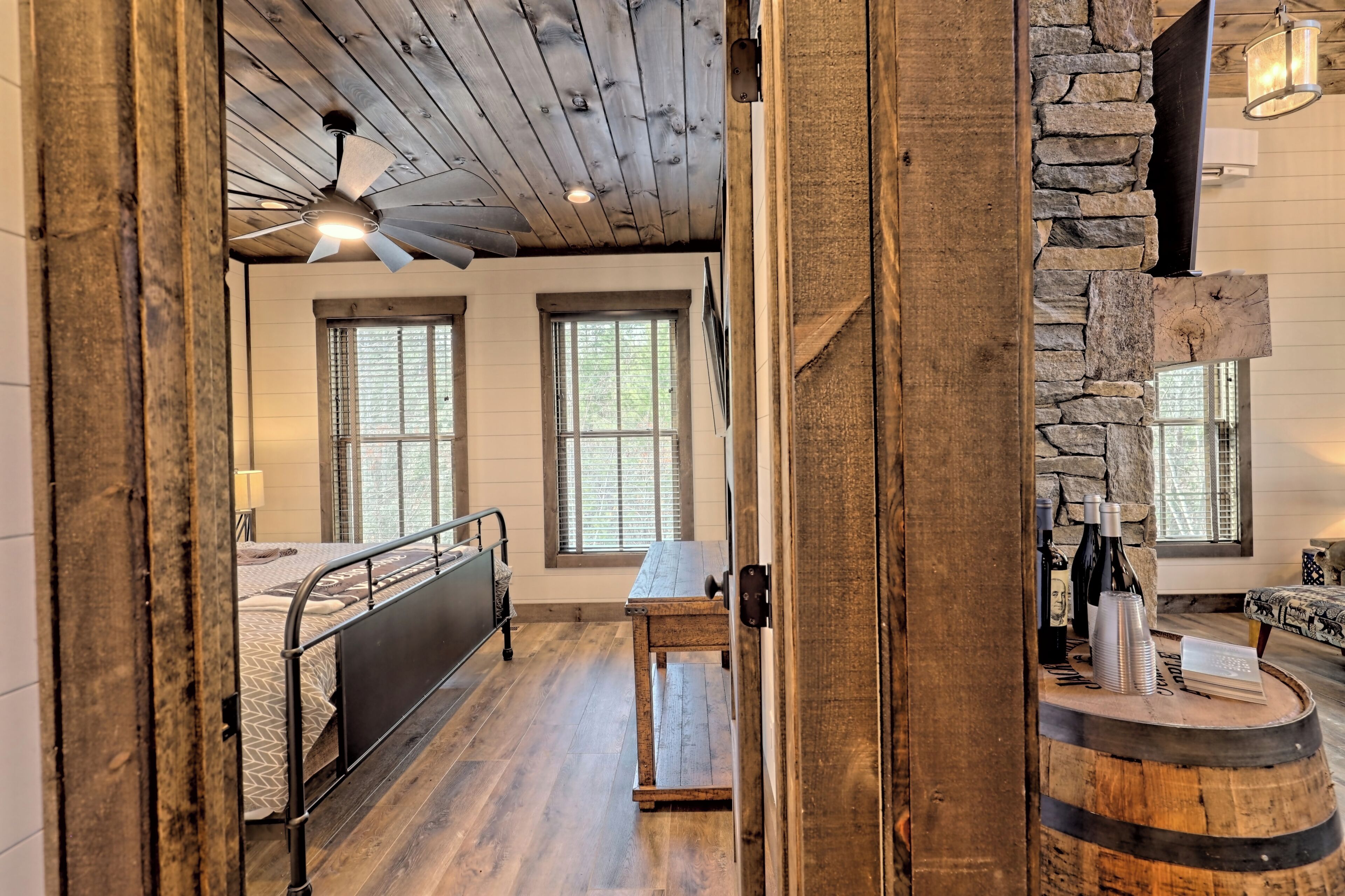 Une chambre à coucher rustique avec un lit, une table en bois sur laquelle sont posées des bouteilles, et un mur en pierre.