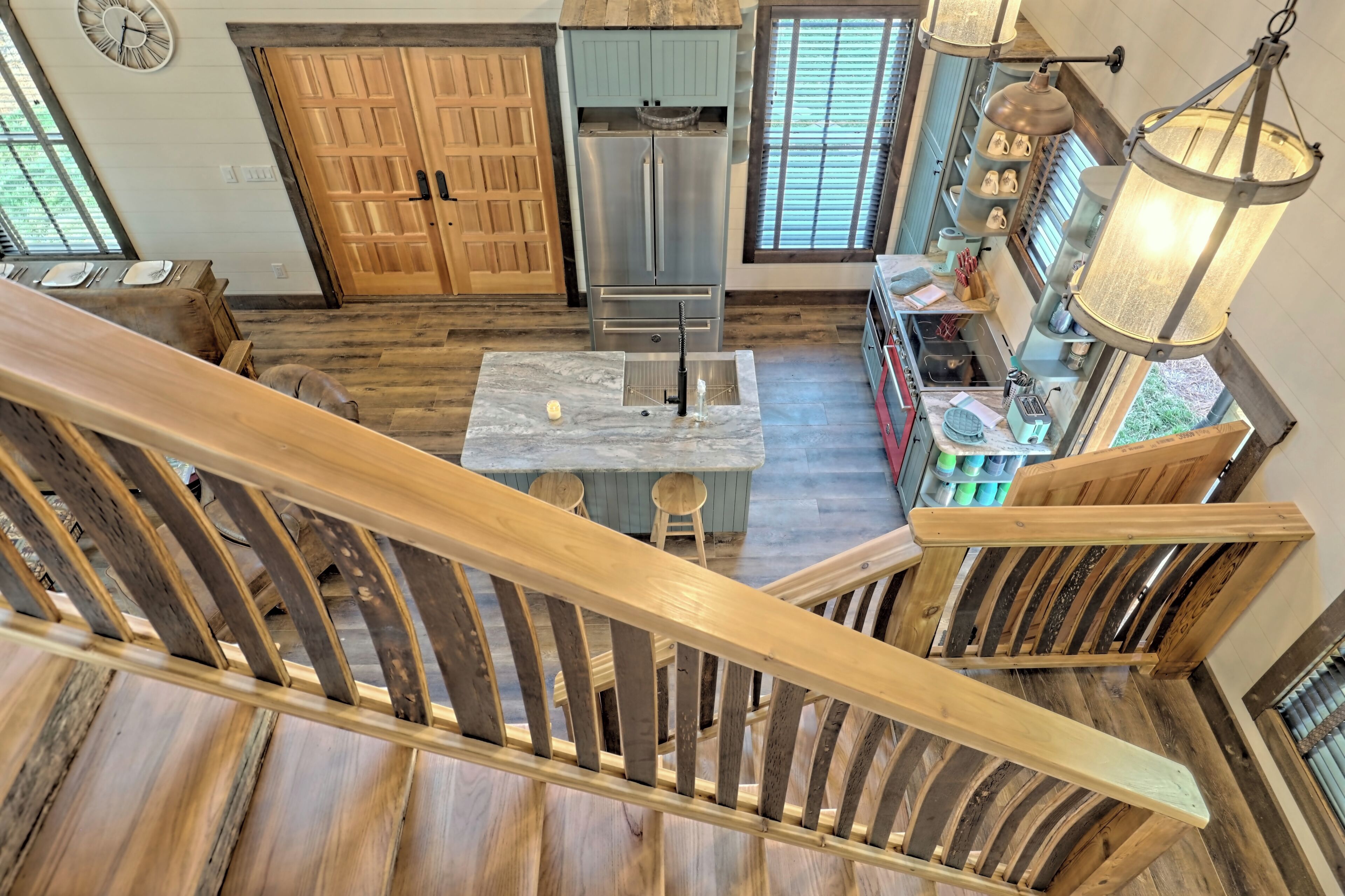 Une cuisine avec un escalier en bois, un réfrigérateur en acier inoxydable et un luminaire suspendu.
