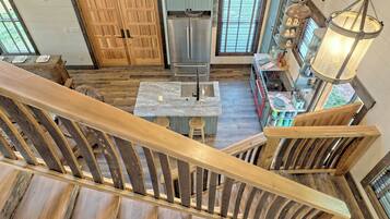 A kitchen with a wooden staircase, a stainless steel refrigerator, and a hanging light fixture.