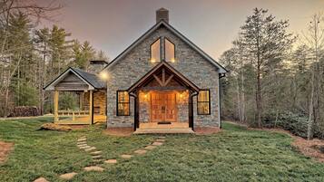 A two-story stone house with a prominent front entrance, a covered porch, and a stone chimney.
