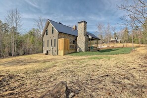 Ein zweistöckiges Haus mit einem Steinsschornstein, einer Holzterrasse und einem überdachten Außenbereich mit Sitzgelegenheiten.