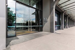 A modern building entrance with glass doors, a metal sign with the letter 'M', and a covered walkway. - Mariner Resort Style Escape Where City meets Coast (Port Melbourne)