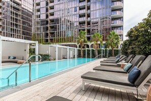 A poolside area with lounge chairs and a swimming pool, surrounded by a modern building with balconies. - Mariner Resort Style Escape Where City meets Coast (Port Melbourne)