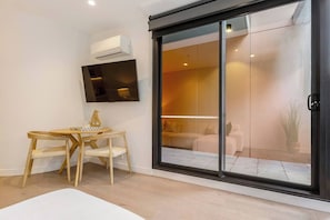 Ein modernes Wohnzimmer mit flachbildfernseher an der Wand, einem Holzesstisch mit Stühlen und einer Glastür, die auf einen Balkon mit einer Couch und einer Pflanze führt.