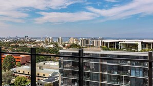 A high-rise building with multiple floors, large windows, and a view of a cityscape with various buildings and a body of water in the distance. - Mariner Resort Style Escape Where City meets Coast (Port Melbourne)