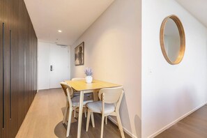 A hotel room with a wooden dining table, four chairs, a vase with flowers, a painting on the wall, and a round mirror. - The Parkhouse Riverside Living with Pool and Sauna (Abbotsford)