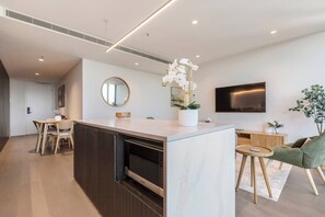A modern kitchen with a marble countertop, wooden cabinets, a central island with a white orchid, a round mirror, and a flat-screen TV mounted on the wall. - The Parkhouse Riverside Living with Pool and Sauna (Abbotsford)