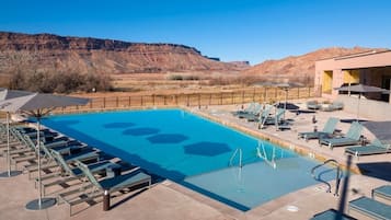 A pool with lounge chairs, a poolside area, and a mountain backdrop.