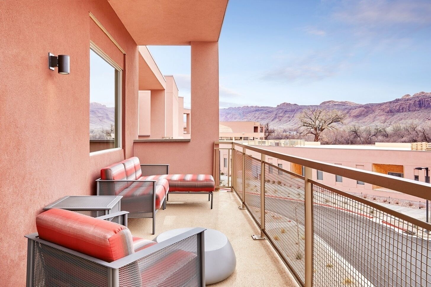 Un balcon avec des sièges pour l’extérieur, une vue sur un paysage montagneux et un espace délimité par une clôture.