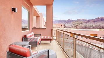 A balcony with outdoor seating, a view of a mountainous landscape, and a fenced area.