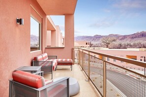 A balcony with outdoor seating, a view of a mountainous landscape, and a fenced area.