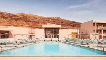 A pool area with lounge chairs, a building with a modern design, and a mountainous backdrop.